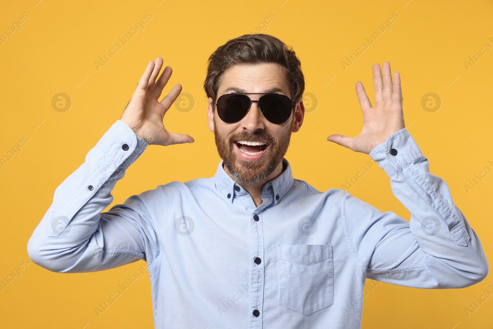 Photo of Portrait of excited bearded man with stylish sunglasses on orange background