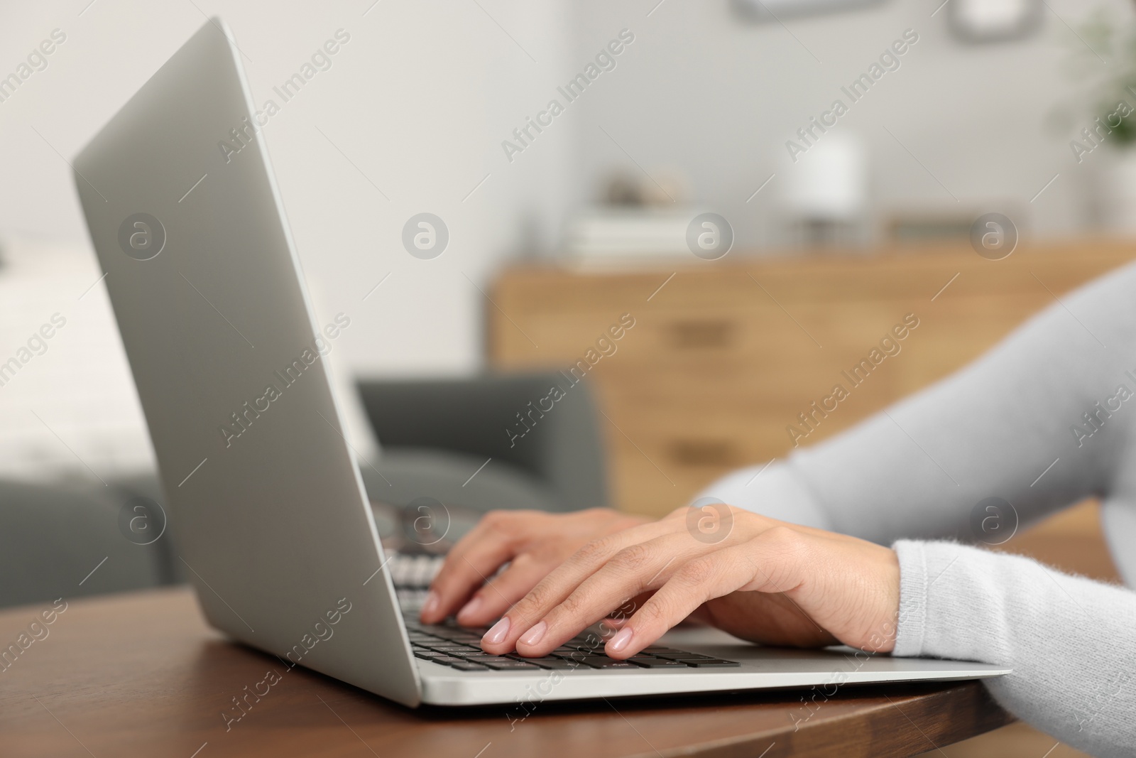 Photo of Woman using laptop at wooden coffee table in room, closeup