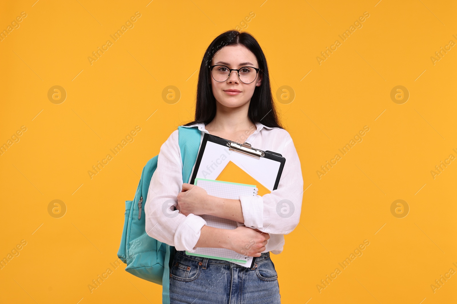 Photo of Student with notebooks and clipboard on yellow background