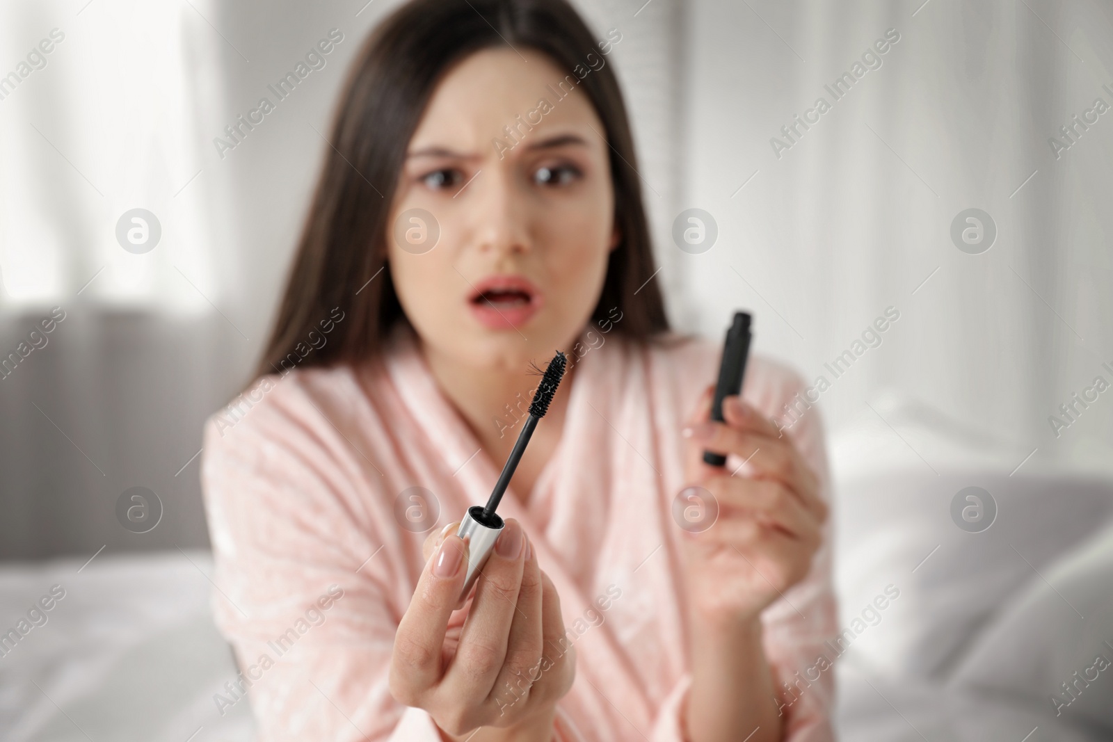 Photo of Beautiful woman holding mascara brush with fallen eyelashes indoors