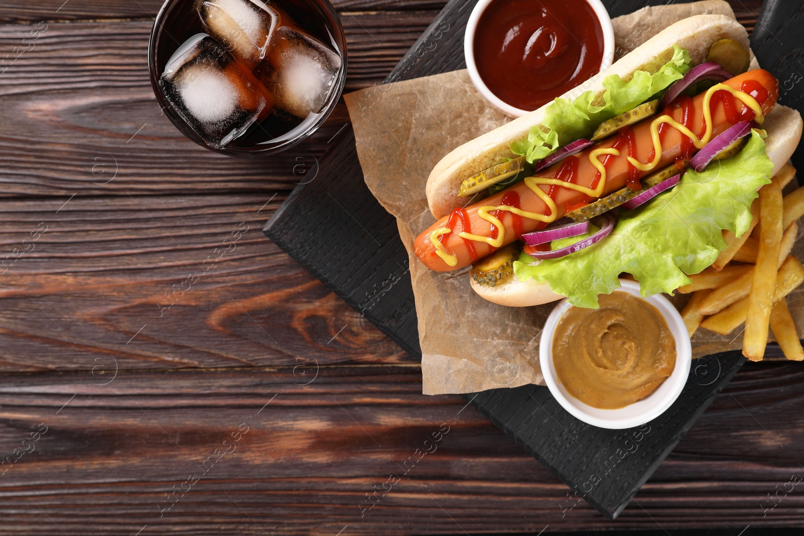 Photo of Delicious hot dog with lettuce, onion and pickle served on wooden table, top view. Space for text