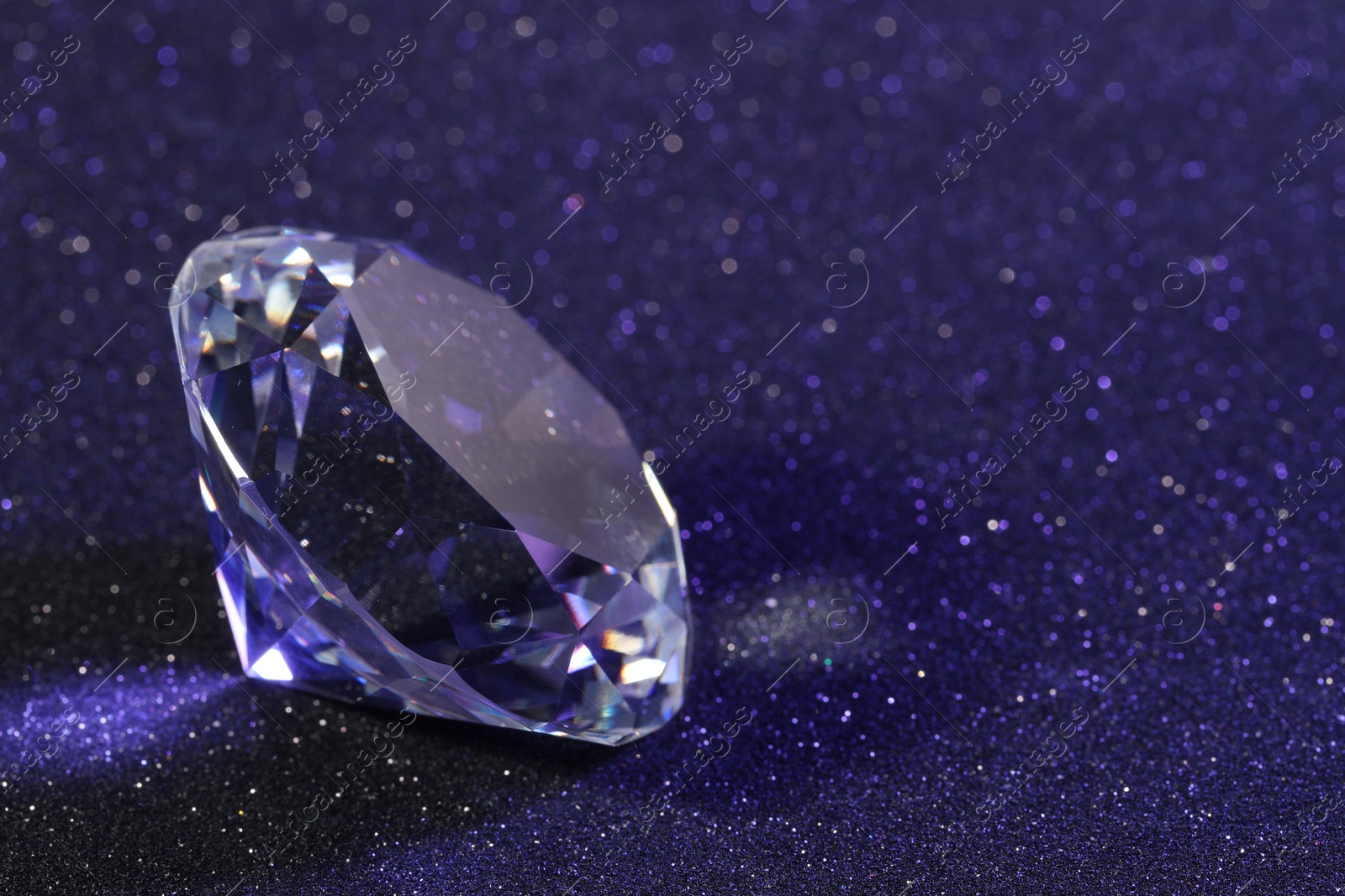 Photo of Beautiful dazzling diamond on violet glitter background, closeup. Space for text