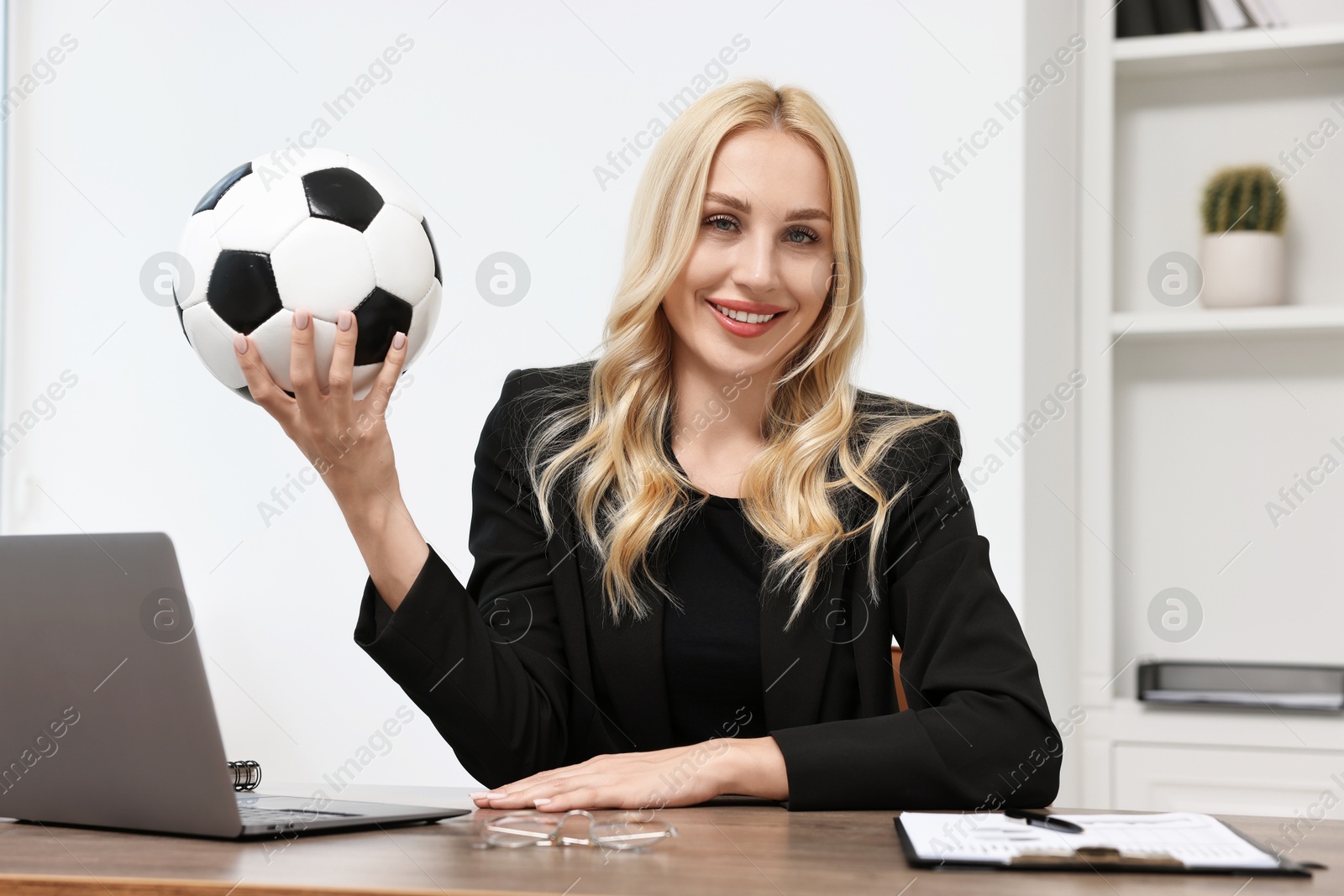 Photo of Happy woman with soccer ball at table in office