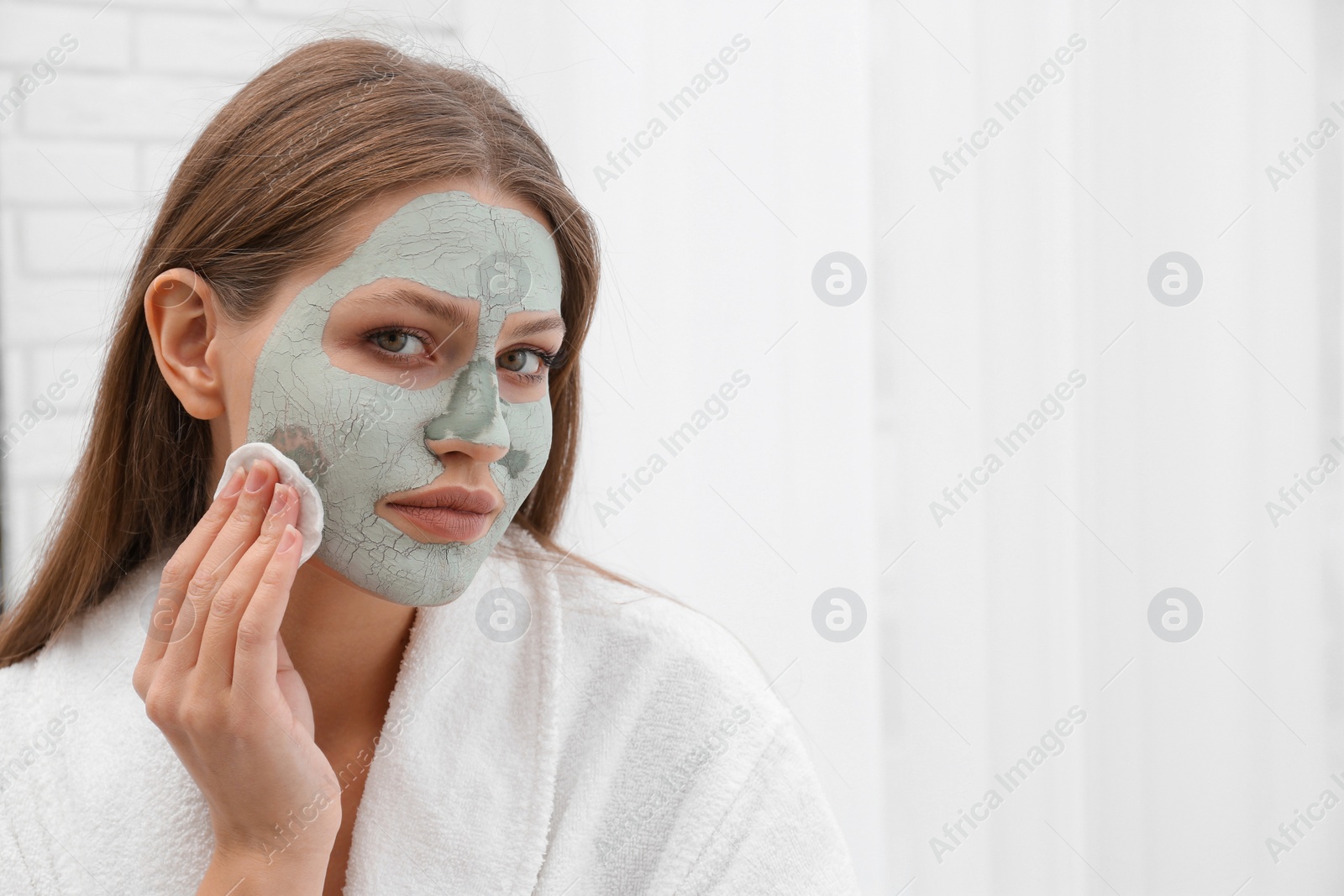 Photo of Beautiful woman removing clay mask from her face indoors