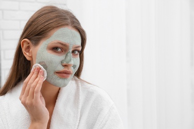 Photo of Beautiful woman removing clay mask from her face indoors