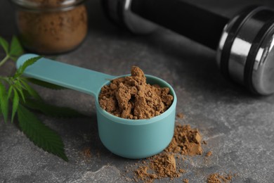 Photo of Hemp protein powder, fresh leaves and dumbbell on grey table, closeup