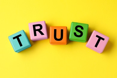 Photo of Word Trust made of colorful cubes on yellow background, flat lay