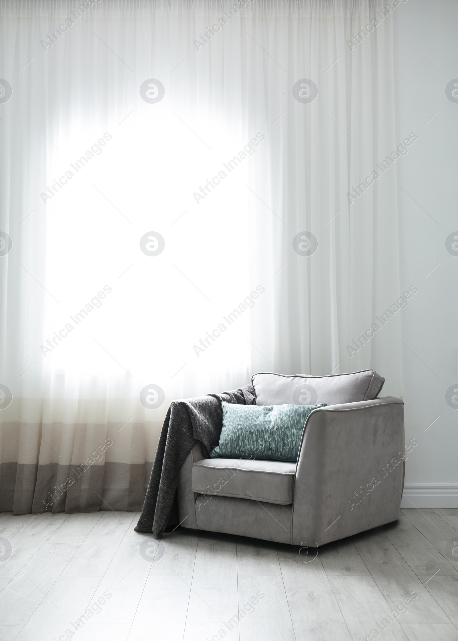 Photo of Cozy armchair with pillows and plaid near window in room. Interior design