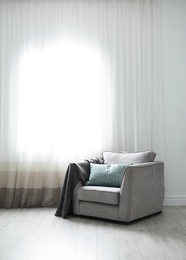 Cozy armchair with pillows and plaid near window in room. Interior design