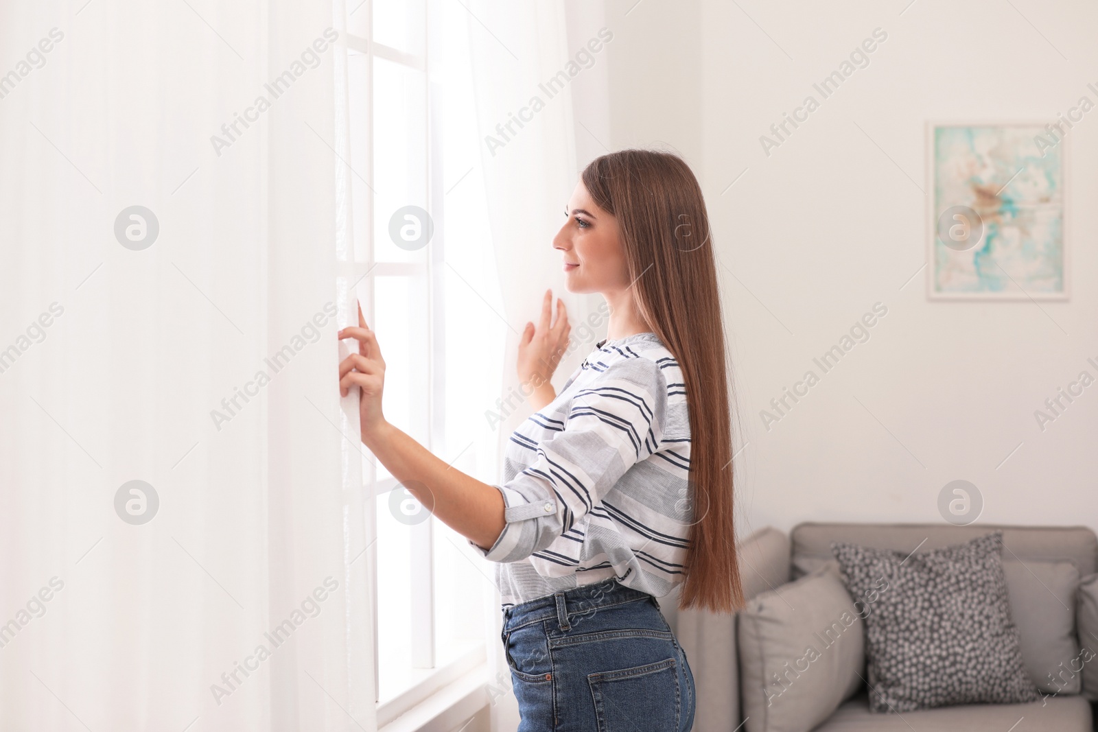 Photo of Young woman opening window curtains at home. Space for text