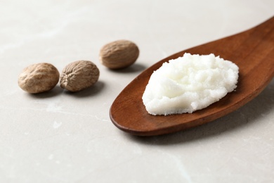 Shea butter in wooden spoon and nuts on table. Space for text