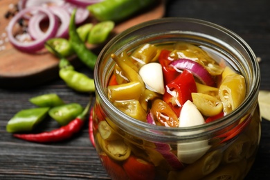 Glass jar with pickled peppers on wooden table, closeup