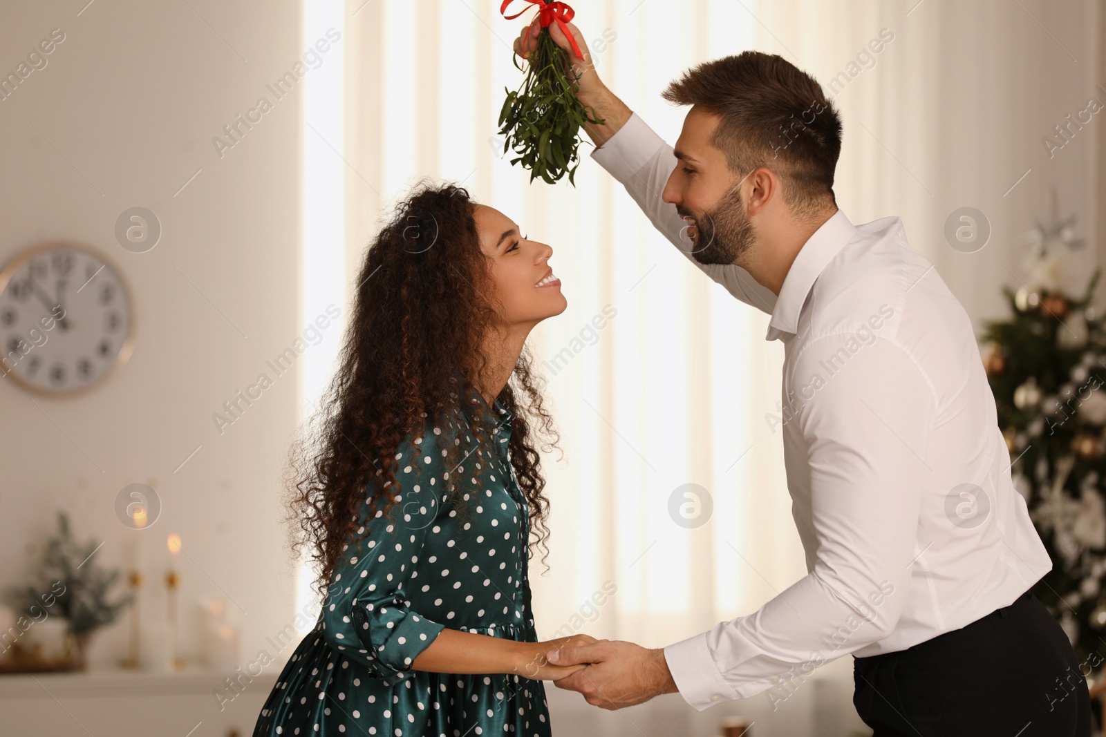 Photo of Lovely couple under mistletoe bunch in room decorated for Christmas