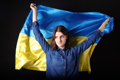 Photo of Young woman holding Ukrainian flag on black background