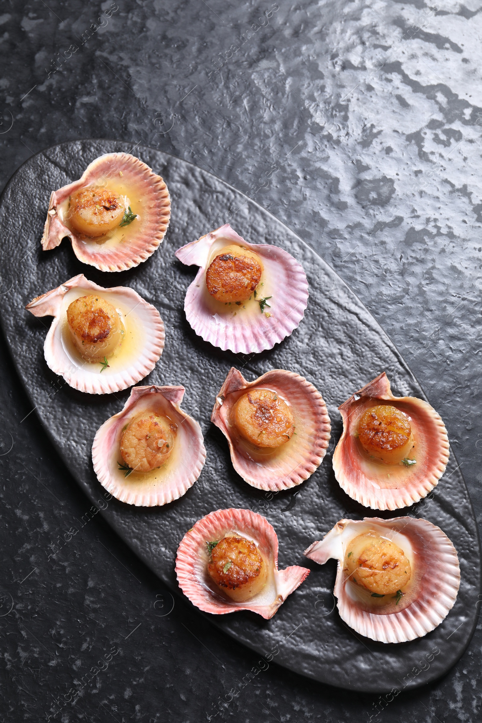 Photo of Delicious fried scallops in shells on black table, top view