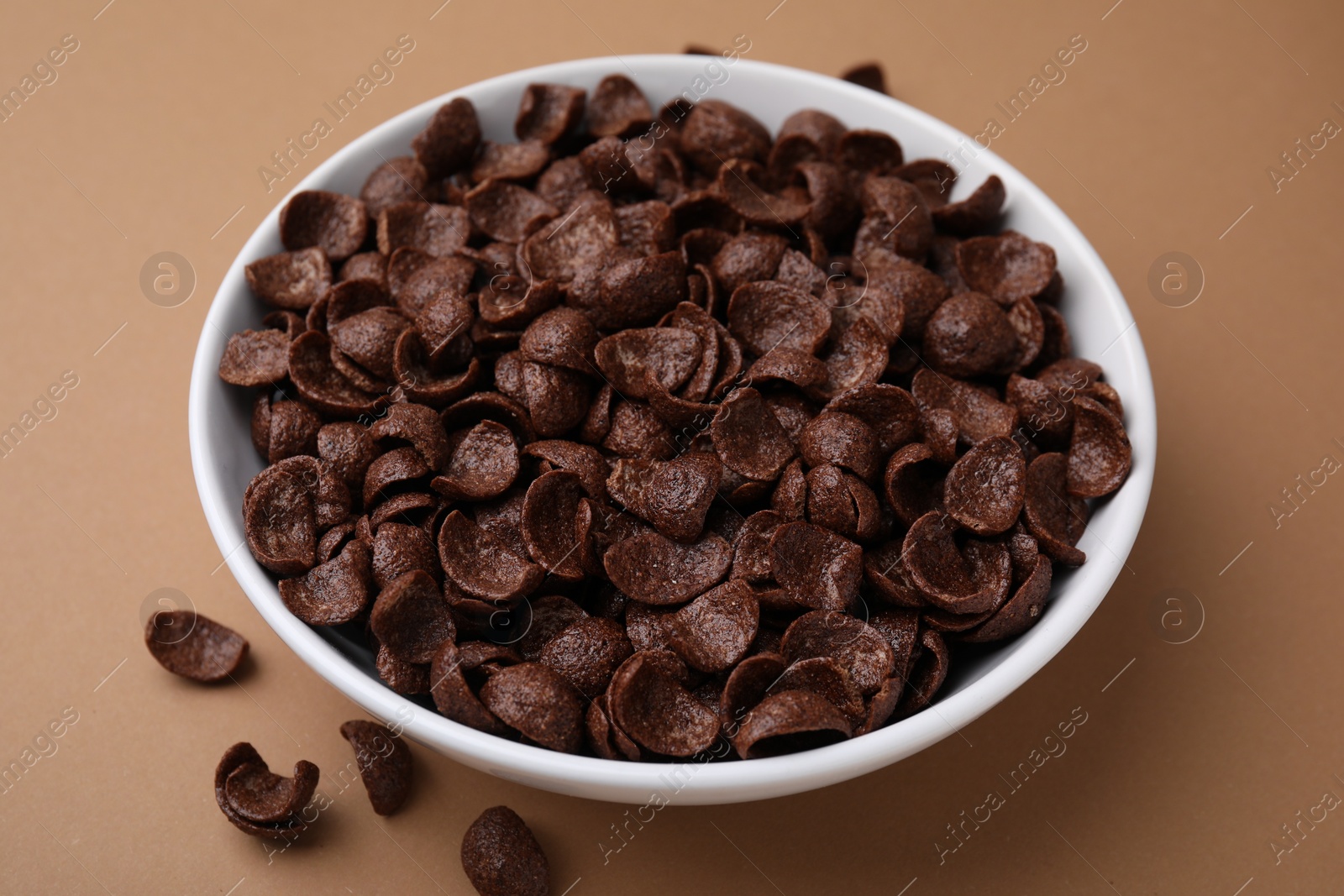 Photo of Breakfast cereal. Chocolate corn flakes in bowl on brown table, closeup