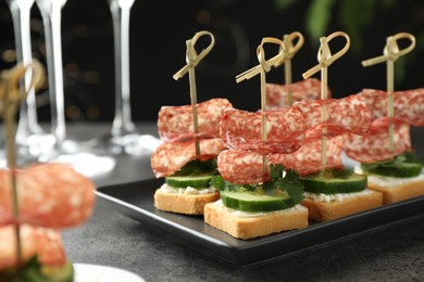 Photo of Tasty canapes with salami, cucumber and cream cheese on grey table