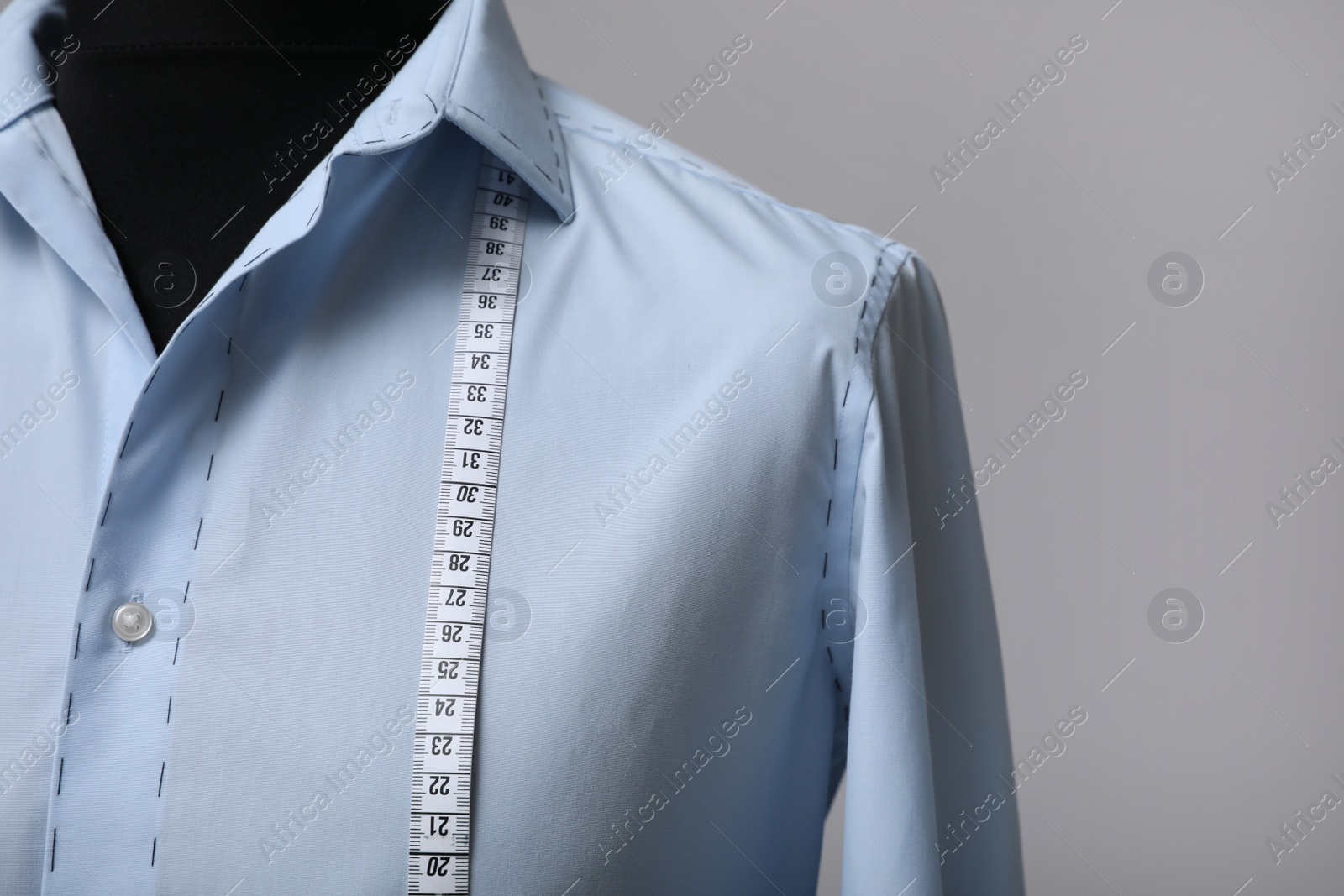 Photo of Semi-ready shirt with tailor's measuring tape on mannequin against grey background, closeup