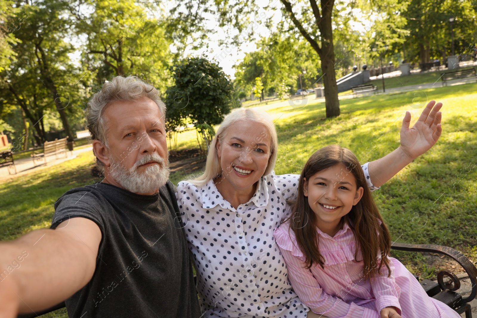 Photo of Happy grandparents with little girl taking selfie in park