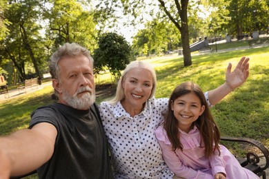 Happy grandparents with little girl taking selfie in park