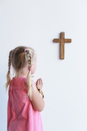 Photo of Little girl with beads praying near light wall