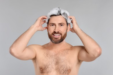 Photo of Happy man washing his hair with shampoo on grey background