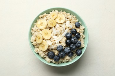 Photo of Tasty oatmeal with banana, blueberries, coconut flakes and honey served in bowl on beige table, top view
