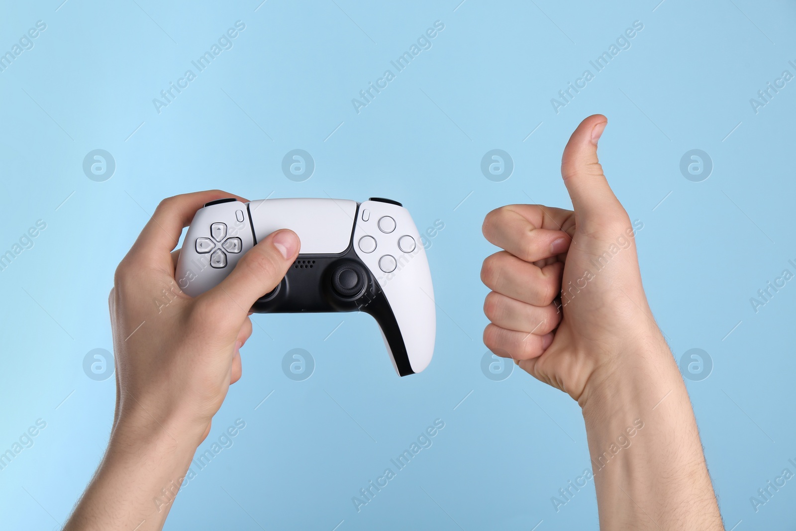 Photo of Man using wireless game controller and showing thumbs up on light blue background, closeup