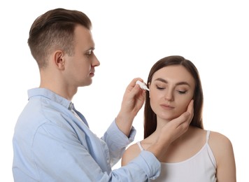Man dripping medication into woman's ear on white background