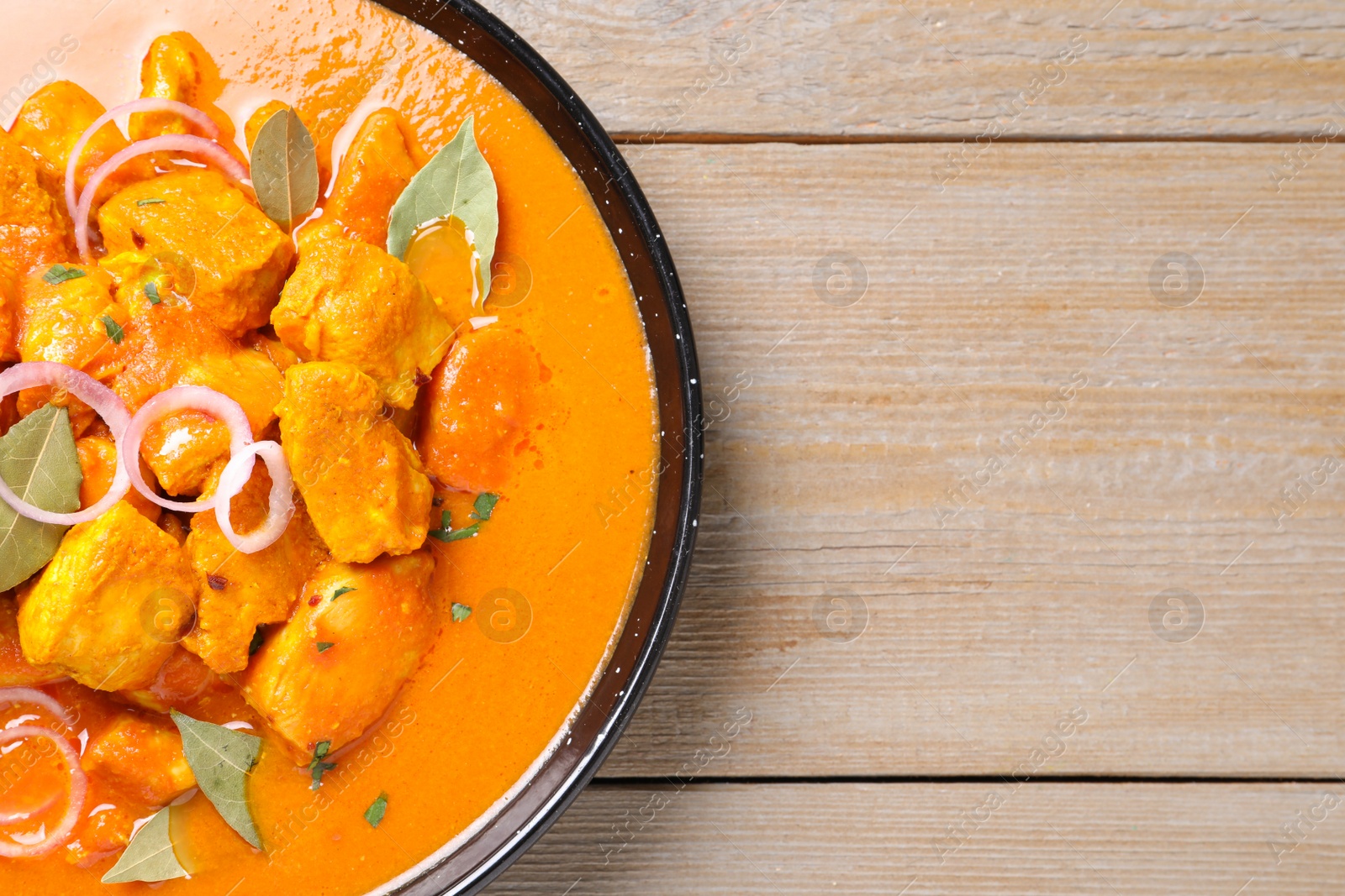 Photo of Delicious chicken curry in pan on wooden table, top view. Space for text