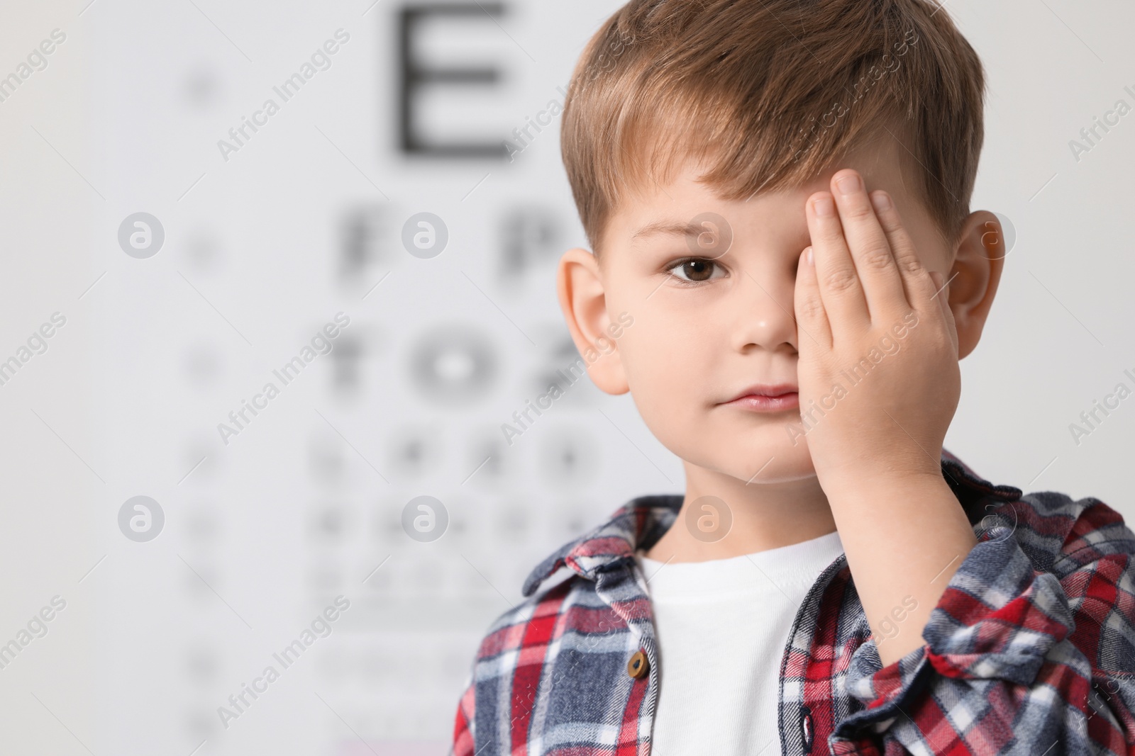 Photo of Little boy covering her eye against vision test chart