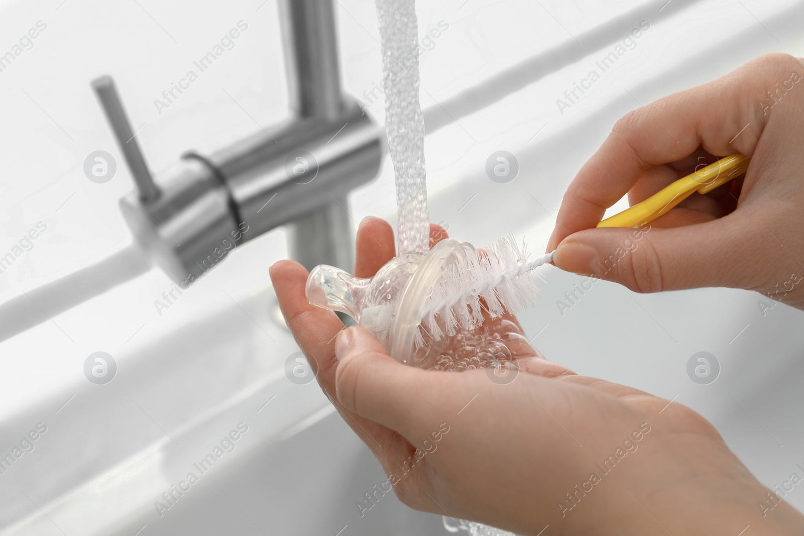 Photo of Woman washing baby bottle nipple under stream of water, closeup