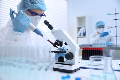 Scientist dripping sample onto glass slide while working with microscope in laboratory