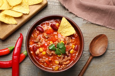 Tasty chili con carne with nachos served on wooden table, flat lay