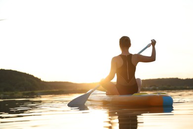 Photo of Woman paddle boarding on SUP board in river at sunset, back view
