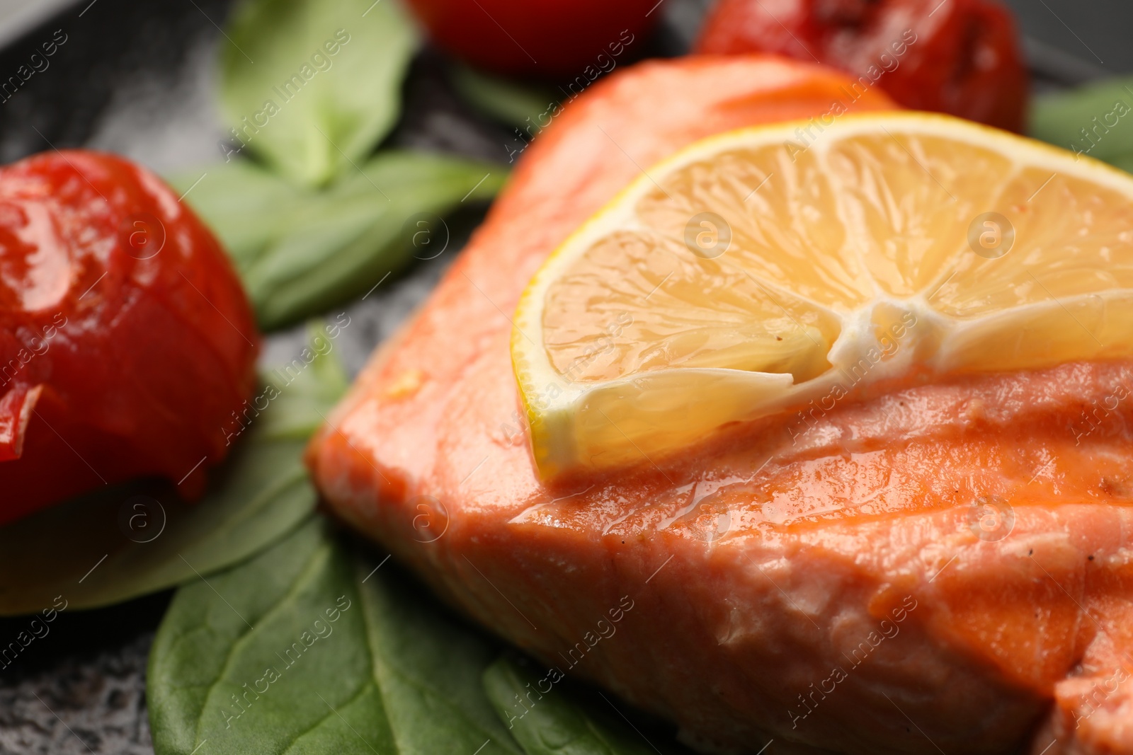 Photo of Tasty grilled salmon with tomatoes, spinach and lemon on plate, closeup