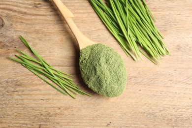 Wheat grass powder in spoon and fresh green sprouts on wooden table, flat lay