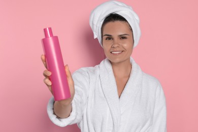 Beautiful young woman holding bottle of shampoo on pink background