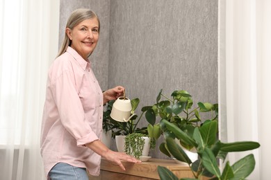 Photo of Happy housewife watering green houseplants at home