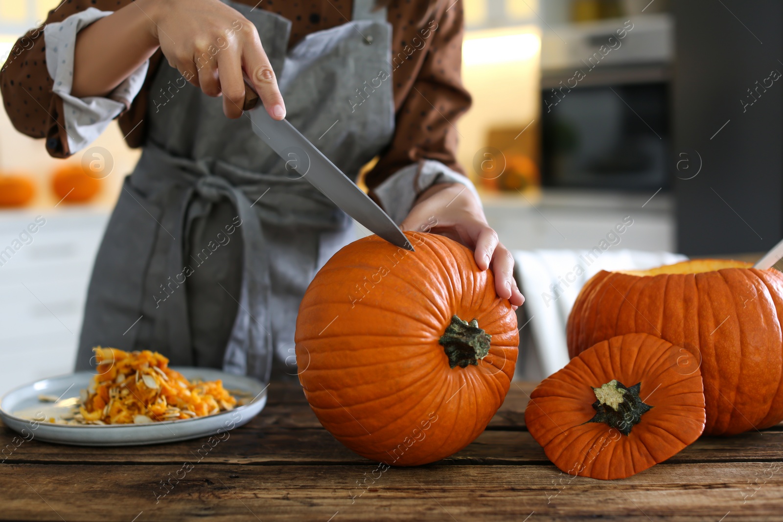 Photo of Woman carving pumpkin at table in kitchen. Halloween celebration