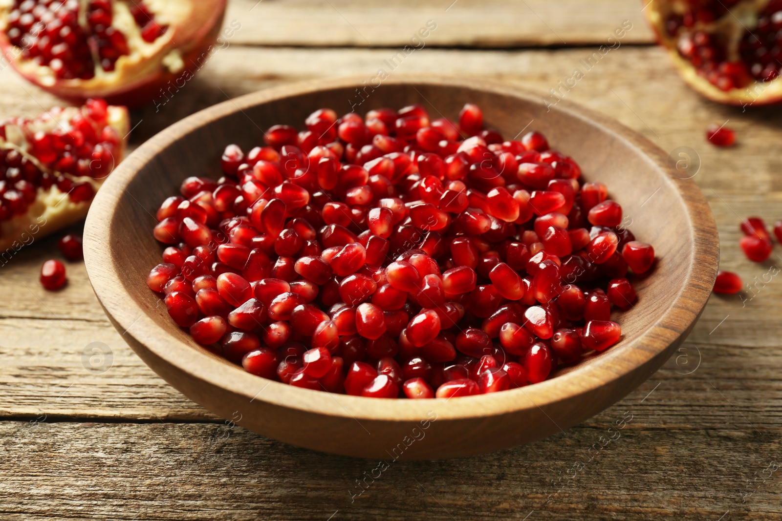 Photo of Ripe juicy pomegranate grains in bowl on wooden table, closeup