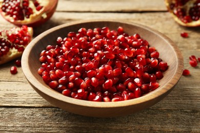 Ripe juicy pomegranate grains in bowl on wooden table, closeup