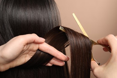 Hairdresser cutting client's hair with scissors on beige background, closeup