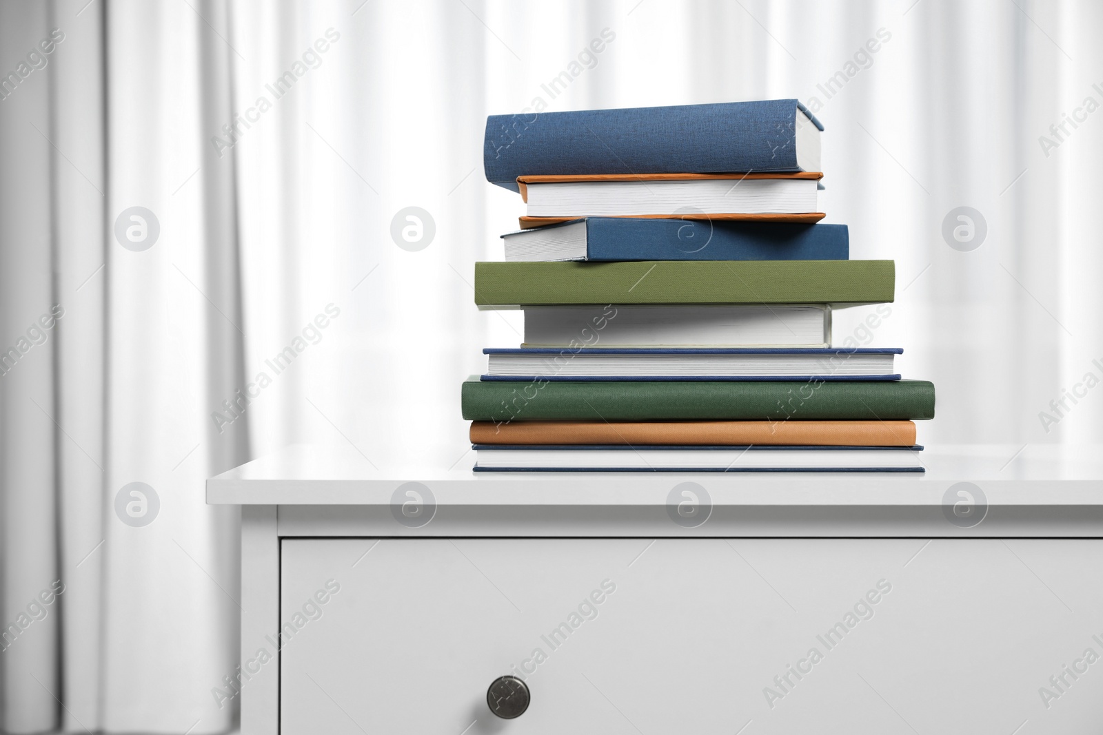 Photo of Hardcover books on white chest of drawers indoors