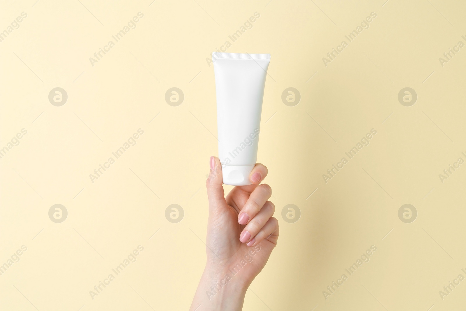 Photo of Woman holding tube of cream on yellow background, closeup