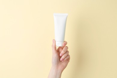 Woman holding tube of cream on yellow background, closeup