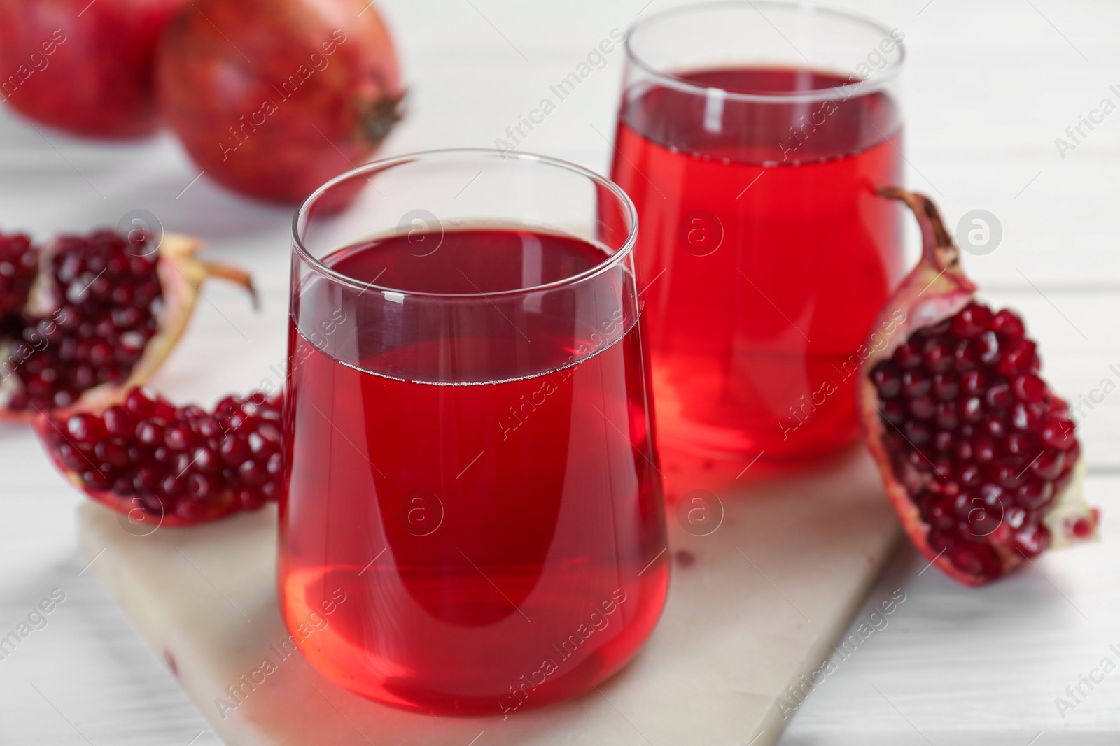 Photo of Tasty pomegranate juice in glasses and fresh fruits on white wooden table, closeup