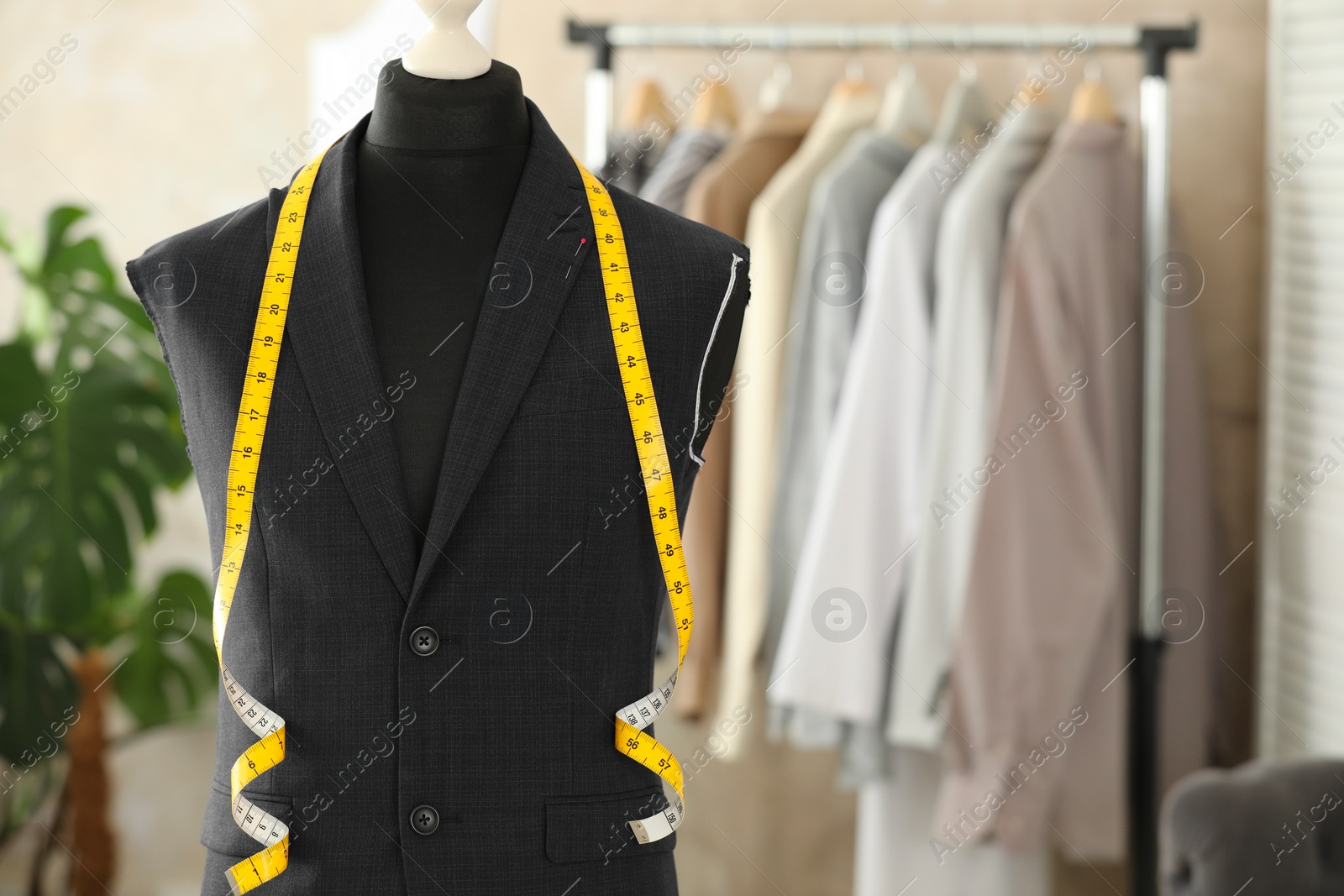 Photo of Mannequin with unfinished suit jacket and measuring tape in tailor shop, space for text