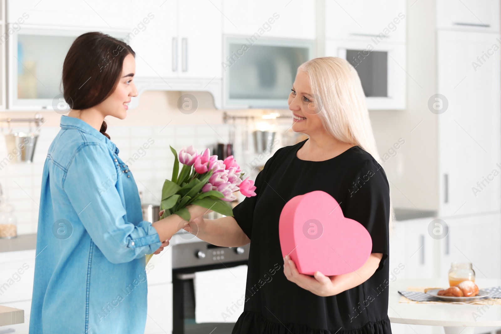 Photo of Daughter congratulating happy mature woman on Mother's Day at home