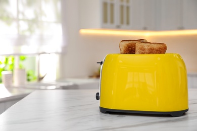Photo of Modern toaster with slices of bread on table in kitchen. Space for text